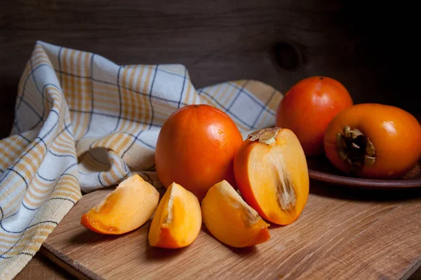 Whole ripe persimmon and sliced fruit on a wooden background — Stock Photo, Image