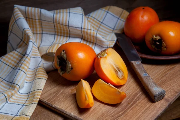 Whole ripe persimmon and sliced fruit on a wooden background — Stock Photo, Image