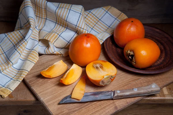 Whole ripe persimmon and sliced fruit on a wooden background — Stock Photo, Image