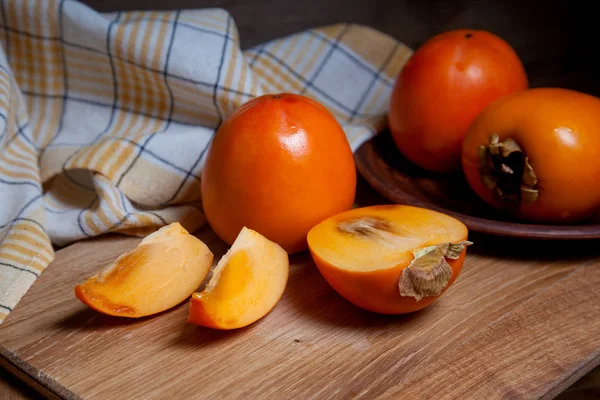 Whole ripe persimmon and sliced fruit on a wooden background — 스톡 사진