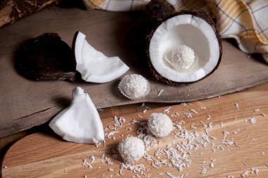 Hindistan cevizini beyaz hamurlu, hindistan cevizli ve tatlı hindistancevizli trüf mantarlı kapat. Hindistan cevizi kabuğu, hindistan cevizi taneleri, kırılmış fındık parçaları, hindistan cevizi kırıntısı ve ahşap arka planda beyaz hindistan cevizi tatlısı..