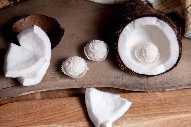 Hindistan cevizi ve hindistan cevizli tatlı mantarlar. Hindistan cevizi kabuğu, hindistan cevizi taneleri, küçük parçalanmış fındık parçaları ve ahşap arka planda beyaz hindistan cevizi tatlısı. Kabuğunda tropik meyve hindistancevizi.