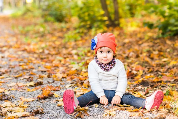 Pequena menina bonito sentado em folhas amarelas — Fotografia de Stock