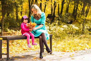 Küçük kız ve annesi sonbahar parkında oynuyorlar.