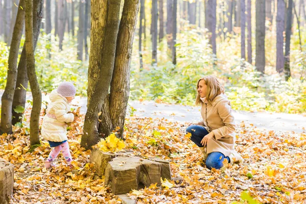 Feliz familia madre y niño niña jugando tiro hojas en otoño parque al aire libre — Foto de Stock