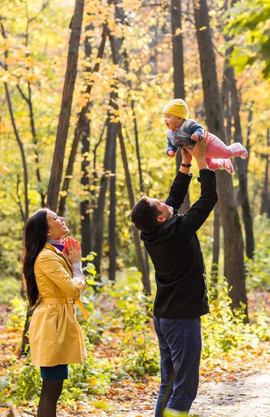 Счастливая молодая семья с дочкой проводят время на свежем воздухе в осеннем парке — стоковое фото