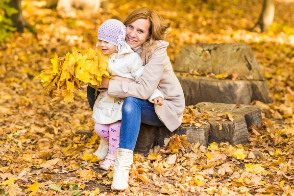 Счастливая мать семьи и ребенок смеются с листьями на природе осенью — стоковое фото