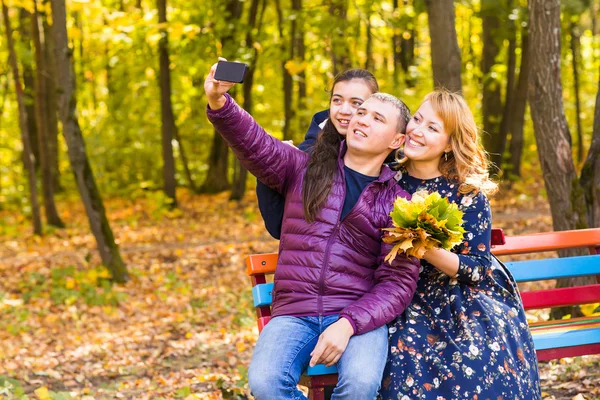 Familie, jeugd, seizoen, technologie en mensen concept - fotograferen in herfst park en gelukkige familie — Stockfoto