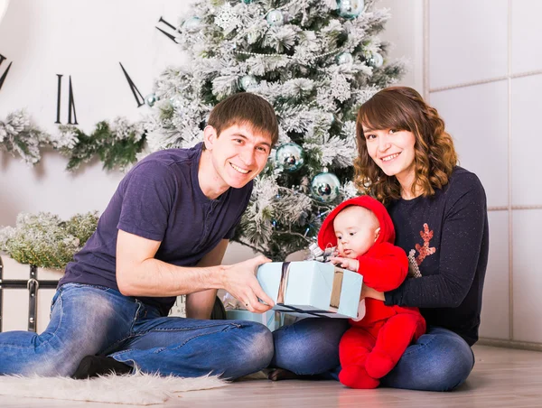 Familia feliz sosteniendo regalos de Navidad cerca del árbol de Navidad. Bebé, madre y padre divirtiéndose en casa — Foto de Stock