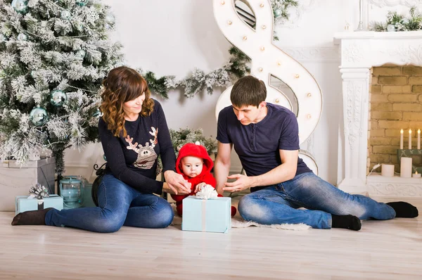 Gelukkige familie bedrijf van de giften van Kerstmis in de buurt van de kerstboom. Baby, moeder en vader plezier thuis — Stockfoto