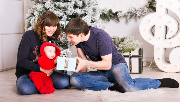 Gelukkige familie bedrijf van de giften van Kerstmis in de buurt van de kerstboom. Baby, moeder en vader plezier thuis — Stockfoto