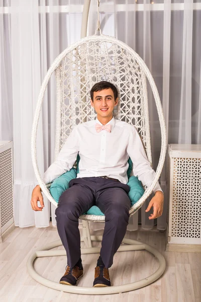 ชายหนุ่มนั่งเก้าอี้สีขาวในห้องสว่าง — ภาพถ่ายสต็อก