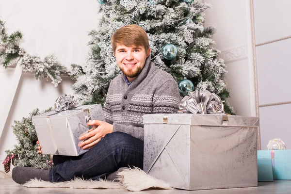 Hombre feliz abriendo un regalo en casa cerca del árbol de Navidad —  Fotos de Stock