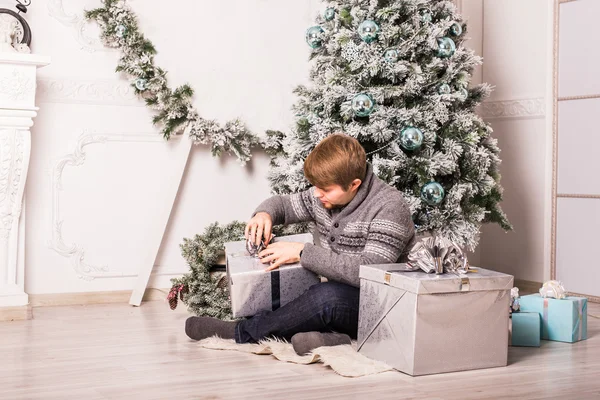 Uomo felice che apre un regalo a casa vicino all'albero di Natale — Foto Stock