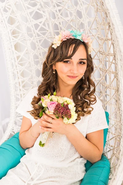 Menina posando em uma coroa decorativa de flores artificiais e buquê dentro de casa — Fotografia de Stock