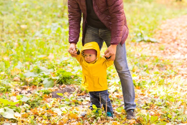 Vader en zoon lopen. Baby die de eerste stappen met hulp van de vader in het najaar tuin in de stad — Stockfoto