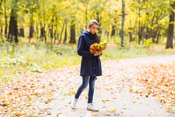 Giovane bella ragazza felice adolescente donna tenendo bouquet di foglie autunnali e sorridente, sullo sfondo della foresta — Foto Stock