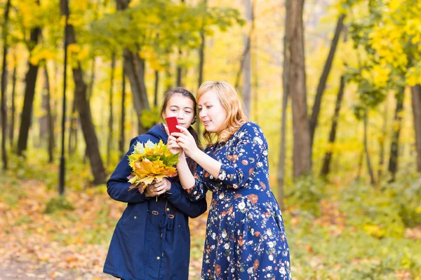 Mãe mostrando suas fotos da menina adolescente no telefone celular ao ar livre na natureza outono — Fotografia de Stock