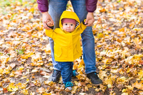 Padre e Hijo caminando. Bebé dando los primeros pasos con la ayuda del padre en el jardín de otoño en la ciudad — Foto de Stock