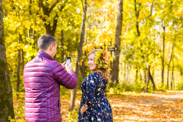 Ung man tar foto av hennes flickvän med mobiltelefon i höstens natur — Stockfoto