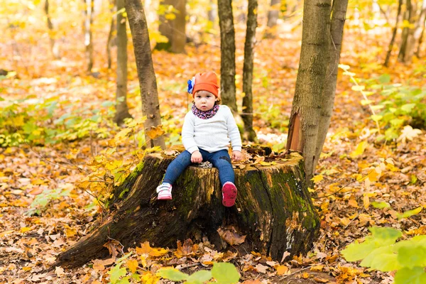 Baby flicka sitter på stubben i höst park utomhus — Stockfoto