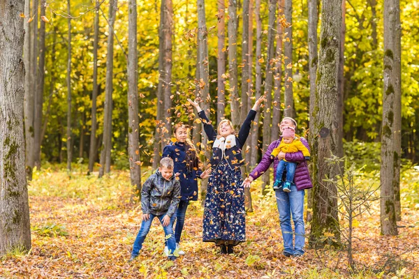 Família, infância, conceito de estação e pessoas - família feliz brincando com folhas de outono no parque — Fotografia de Stock