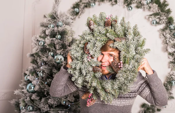 Happy young man and Christmas wreath at home — Stockfoto