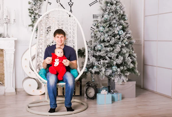 Portret van gelukkige jonge vader zitten in de stoel en het spelen met zijn zoontje in de buurt van de kerstboom — Stockfoto