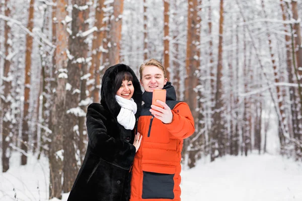 Mensen, seizoen, liefde, technologie en recreatieve concept - gelukkige paar nemen foto met smartphone op over winter achtergrond — Stockfoto