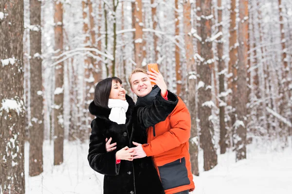 Pessoas, temporada, amor, tecnologia e conceito de lazer - casal feliz tirar fotos com smartphone em fundo de inverno — Fotografia de Stock