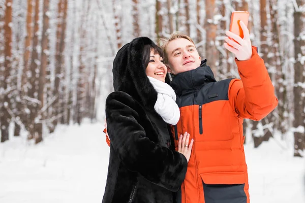 Personnes, saison, amour, technologie et concept de loisirs - couple heureux prenant des photos avec smartphone sur fond d'hiver — Photo