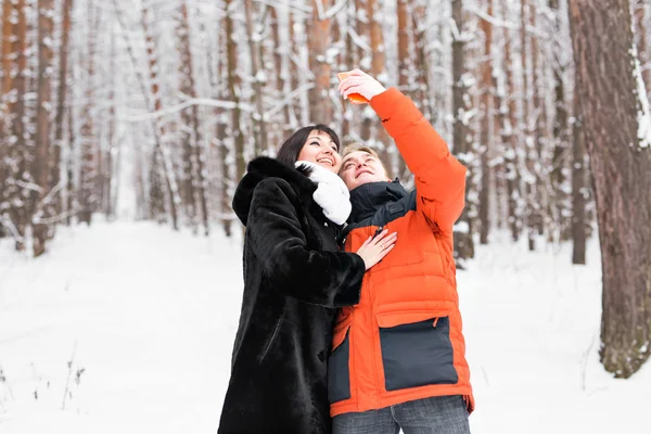 Pessoas, temporada, amor, tecnologia e conceito de lazer - casal feliz tirar fotos com smartphone em fundo de inverno — Fotografia de Stock