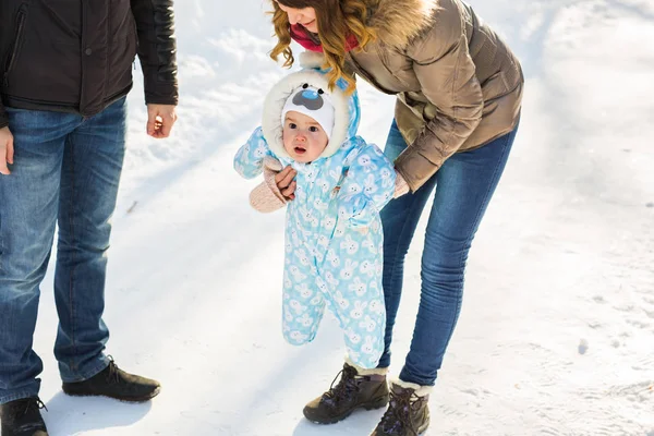 İlk adımlar. Biraz yürümeyi öğrenme bebeğim. Annesi ve babası ile kış parkta yürümeye başlayan çocuk
