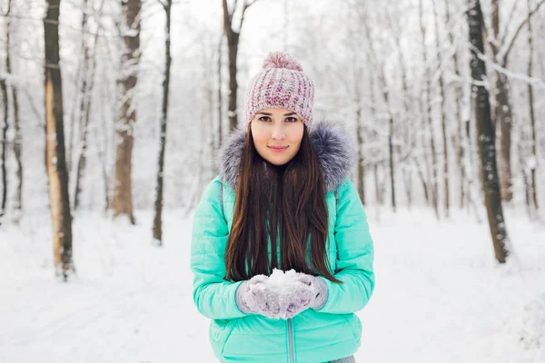 Молода жінка тримає природний м'який білий сніг в руках, щоб зробити снігову кулю, посміхаючись під час холодного зимового дня в лісі, на відкритому повітрі . — стокове фото