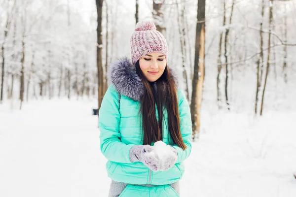 Jovem segurando neve branca macia natural em suas mãos para fazer uma bola de neve, sorrindo durante um dia frio de inverno na floresta, ao ar livre . — Fotografia de Stock