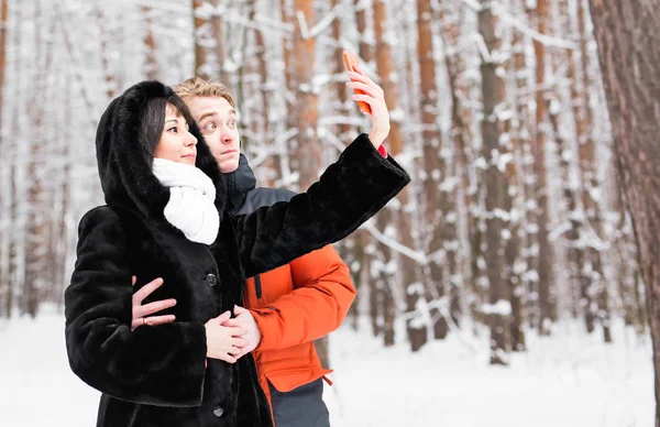 Pessoas, temporada, amor, tecnologia e conceito de lazer - casal feliz tirar fotos com smartphone em fundo de inverno — Fotografia de Stock
