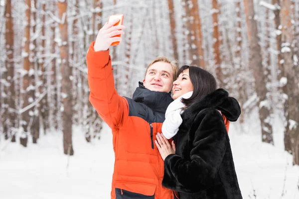 Insanlar, sezon, sevgi, teknoloji ve eğlence kavramı - mutlu çift alarak resmi kış arka plan üzerinde smartphone ile — Stok fotoğraf