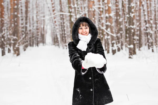 Giovane donna che tiene la neve bianca morbida naturale tra le mani per fare una palla di neve, sorridendo durante una fredda giornata invernale nella foresta, all'aperto . — Foto Stock