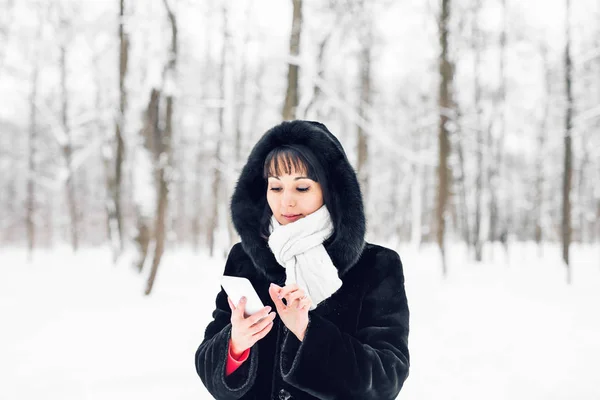 スマートフォンと冬の風景と背景に雪の結晶と笑顔の若い女性 — ストック写真