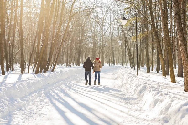 Couple se tenant la main, l'hiver passe sur la route, profitant d'une promenade, d'un couple amoureux. Le mari et la femme traversent le parc en se tenant la main en hiver. La circulation des personnes — Photo