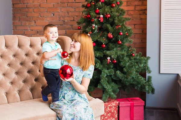 Retrato de mãe feliz e criança segurando bugiganga contra o cenário festivo doméstico com árvore de Natal — Fotografia de Stock
