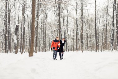 Mutlu çift kışın karlı bir ormanda yürüyor.
