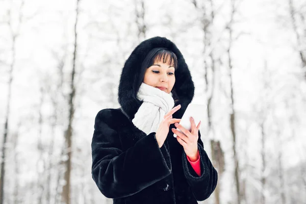 Mujer joven sonriendo con teléfono inteligente y paisaje de invierno — Foto de Stock