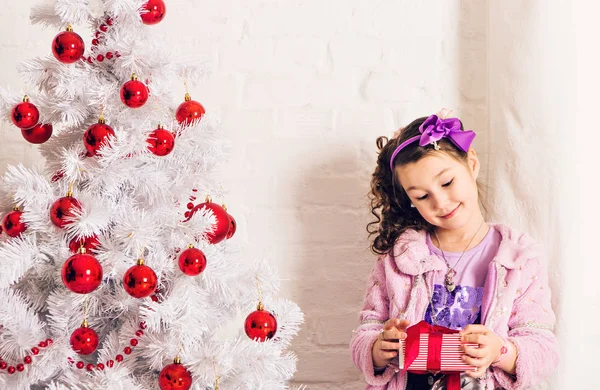 Παιδί με κουτί δώρου δίπλα λευκό χριστουγεννιάτικο δέντρο — Φωτογραφία Αρχείου