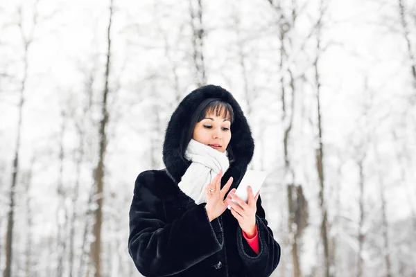 Jovem mulher sorrindo com telefone inteligente e paisagem de inverno — Fotografia de Stock