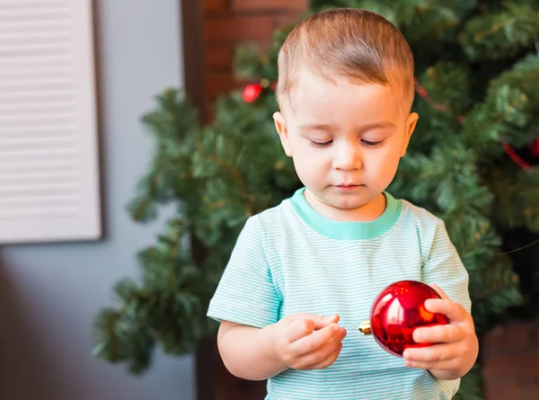 Niño sosteniendo una decoración roja de Navidad . — Foto de Stock
