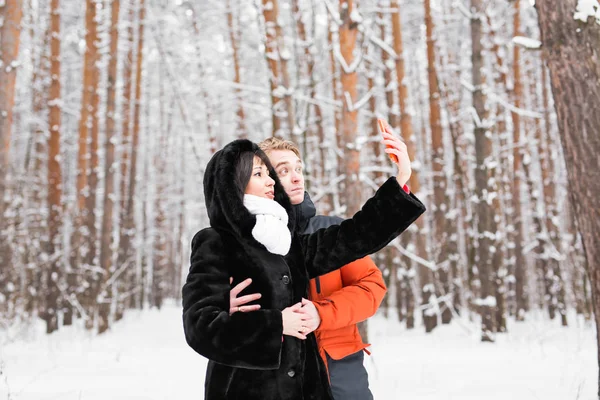 Personas, temporada, amor, tecnología y concepto de ocio - pareja feliz tomando fotos con teléfono inteligente sobre fondo de invierno — Foto de Stock