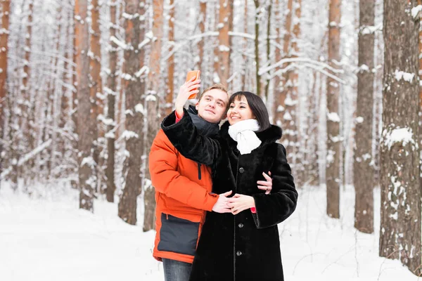 Pessoas, temporada, amor, tecnologia e conceito de lazer - casal feliz tirando fotos com smartphone em fundo de inverno — Fotografia de Stock