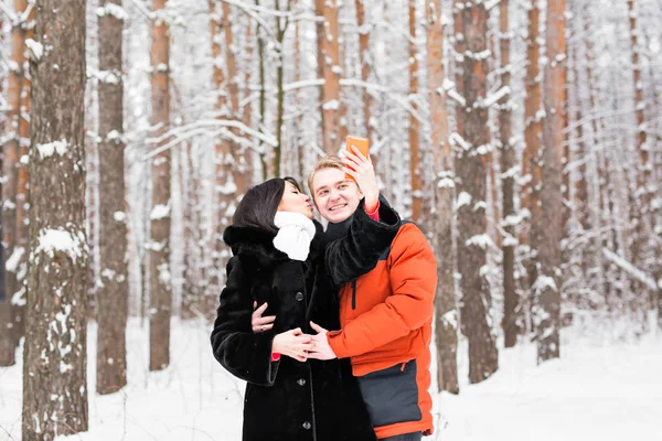 Пара, фотографирующая себя со смартфоном в зимнем парке. Красивое селфи для молодоженов — стоковое фото