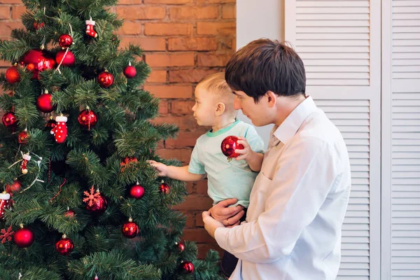 Feliz padre y su hijo bebé decorando el árbol de Navidad en casa . — Foto de Stock